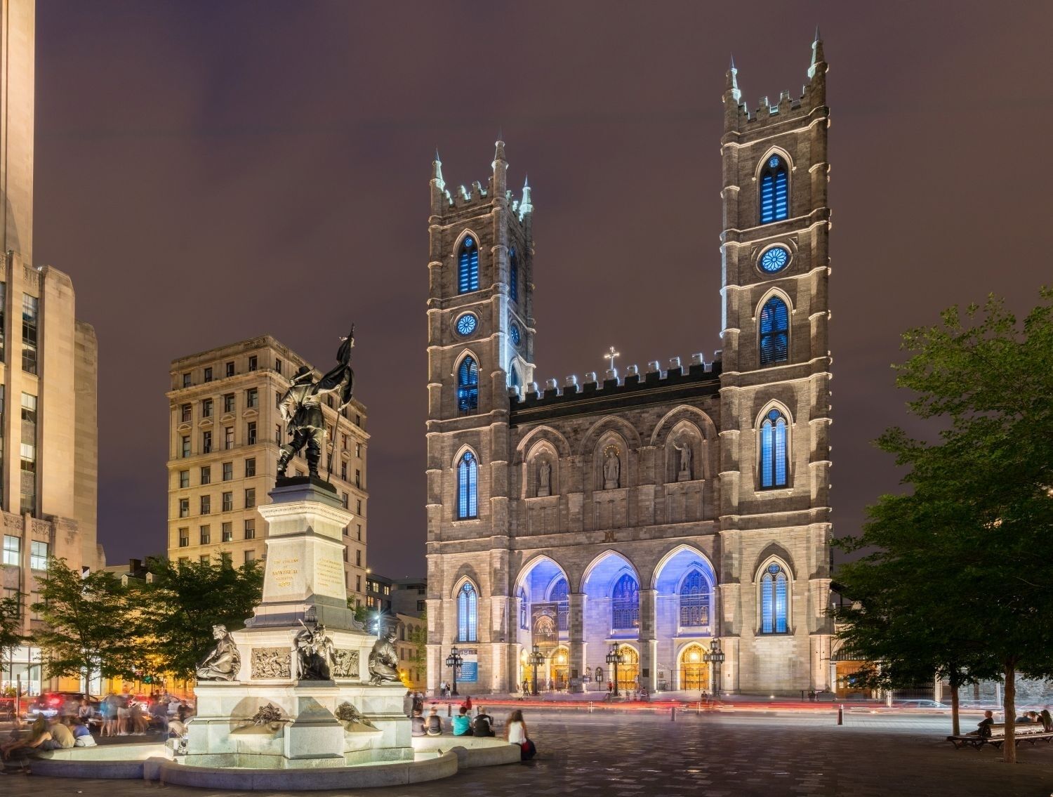 A historic cathedral with twin towers and a central nave, surrounded by a public square with a statue and a fountain.