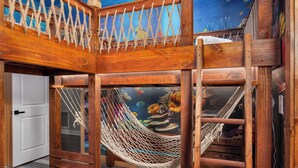 Una terraza de madera con una hamaca, una puerta blanca y una pared con acuario.