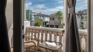 Un balcón con una silla, una mesa y un libro, con vista a una zona residencial con casas y una palmera.