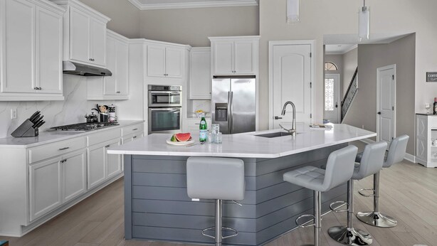 Una cocina moderna con armarios blancos, electrodomésticos de acero inoxidable y una isla central con taburetes de bar.