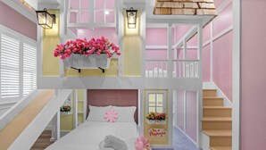 Una habitación de hotel con una cama, un ventanal con persianas, un estante en la pared con flores, una escalera y un letrero que dice "The Playhouse".