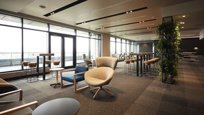 A modern office space with large windows, multiple seating areas, and a central plant.
