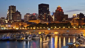 A marina with numerous boats docked, a city skyline in the background, and a waterfront promenade with street lamps. - Enjoy Functional Elegance in Spacious Room w/ Kitchenette + Dining Table (Brossard)