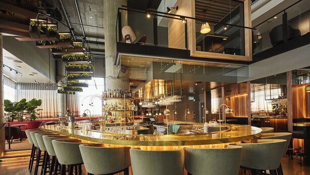 A modern bar area with a central bar, multiple seating options, and a variety of bottles and glasses on display. - Enjoy Functional Elegance in Spacious Room w/ Kitchenette + Dining Table (Brossard)