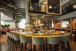 A modern bar area with a central bar, multiple seating options, and a variety of bottles and glasses on display. - Experience Urban Chic Design in Spacious Room Walking Distance to Cafés & Bars (Brossard)