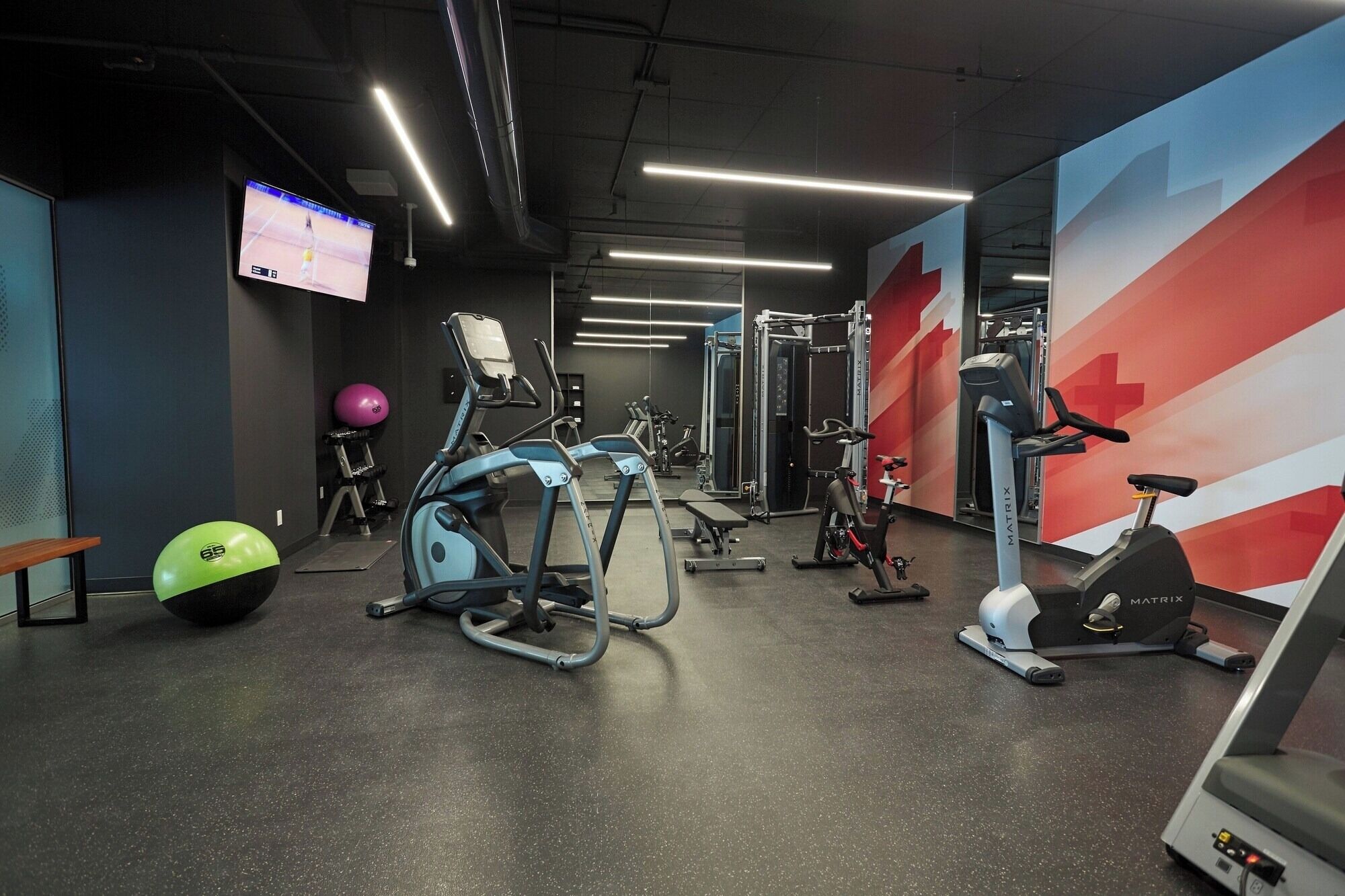 Uma academia com diversos equipamentos de exercícios, incluindo esteiras, uma bicicleta ergométrica e um aparelho de musculação.
