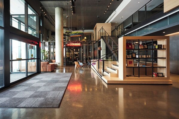 Un intérieur moderne avec un escalier central, un coin salon avec des canapés et une présentation d’objets sur des étagères.