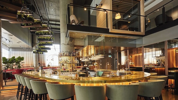 Eine moderne Bar mit einer Theke in der Mitte, verschiedenen Sitzgelegenheiten und einer Auswahl an Flaschen und Gläsern.