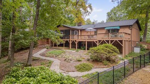 A two-story wooden house with a balcony, surrounded by trees and a gravel pathway. - Nature Lovers Serene Get-A-Way RANCH in North Raleigh (Raleigh)