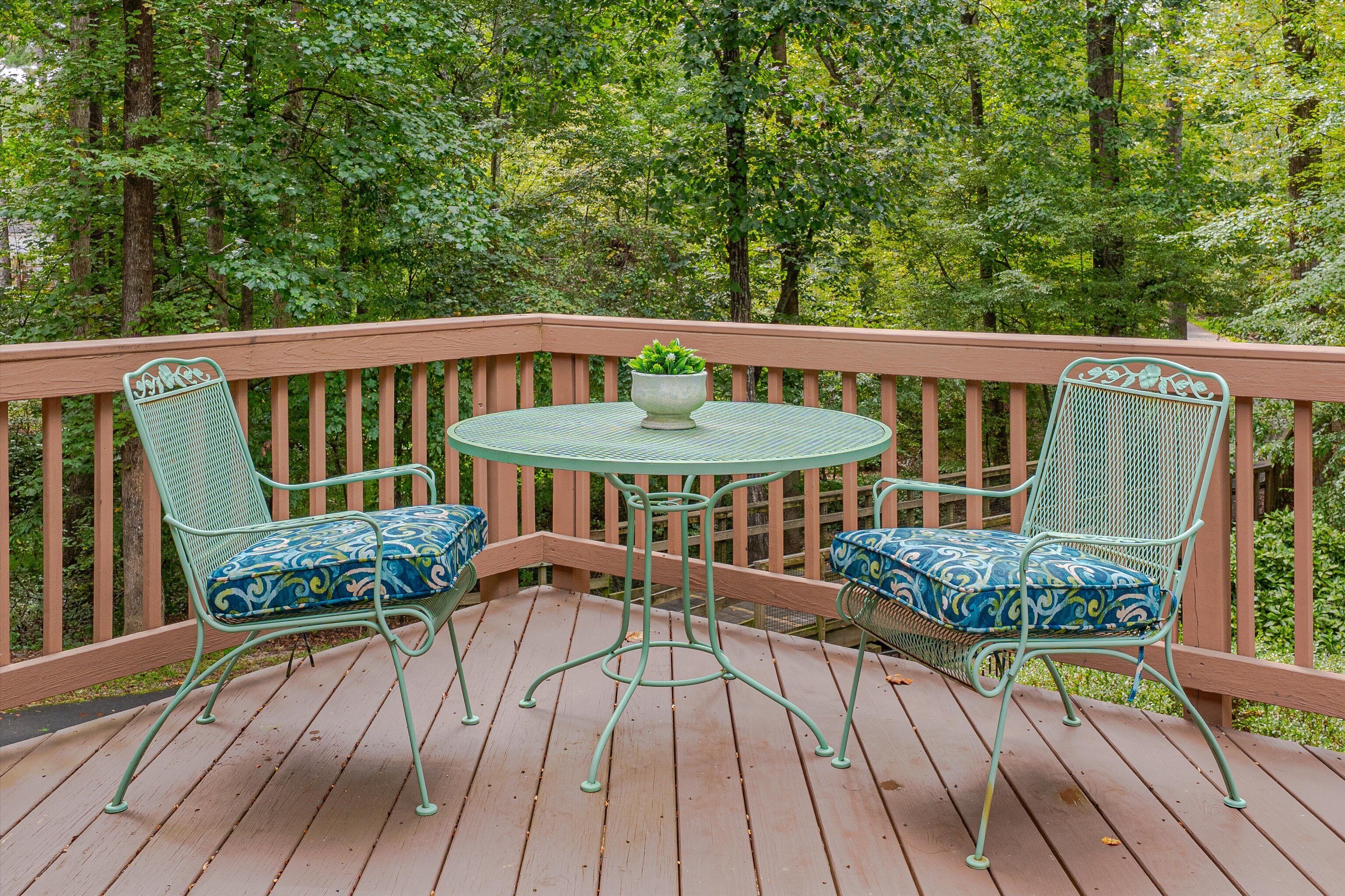 A wooden deck with two green metal chairs and a table, surrounded by a wooden railing.