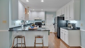 A modern kitchen with white cabinets, a central island with stools, and a refrigerator. - Nature Lovers Serene Get-A-Way RANCH in North Raleigh (Raleigh)