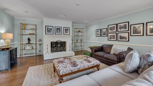 A living room with a fireplace, a sofa, a coffee table, and wall-mounted pictures. - Nature Lovers Serene Get-A-Way RANCH in North Raleigh (Raleigh)