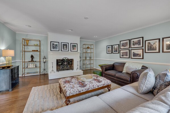 A living room with a fireplace, a sofa, a coffee table, and wall-mounted pictures. - Nature Lovers Serene Get-A-Way RANCH in North Raleigh (Raleigh)