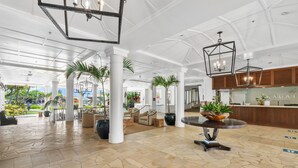 Eine geräumige Lobby mit hoher Decke, weißen Säulen und einer zentralen Sitzgruppe mit einem runden Tisch.