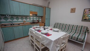 Une cuisine compacte avec des meubles de couleur turquoise, une table à manger pour quatre personnes et un canapé à motifs placé dans un coin.