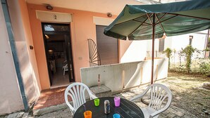 Une terrasse extérieure avec une table ronde, quatre chaises et un parasol vert.