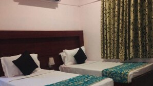 Habitación de hotel con dos camas individuales, cada una con colchón blanco y cubrecama estampado en verde agua. Hay un cabecero de madera sobre las camas y una ventana con cortinas estampadas en verde.