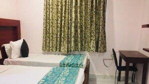 Habitación de hotel con dos camas, cabecero de madera, escritorio con silla y cortina estampada con hojas.