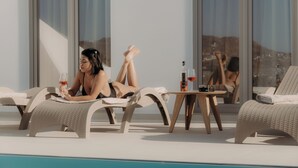 Un espace aménagé au bord de la piscine, avec des chaises longues, une table sur laquelle se trouvent une bouteille et un verre, et une vue sur les montagnes.