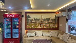 A living room with a sofa, a glass coffee table, a Coca-Cola refrigerator, and a mural on the wall. - Hotel AYODHYA HERITAGE (Ayodhya)