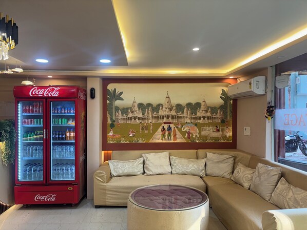 A living room with a sofa, a glass coffee table, a Coca-Cola refrigerator, and a mural on the wall. - Hotel AYODHYA HERITAGE (Ayodhya)