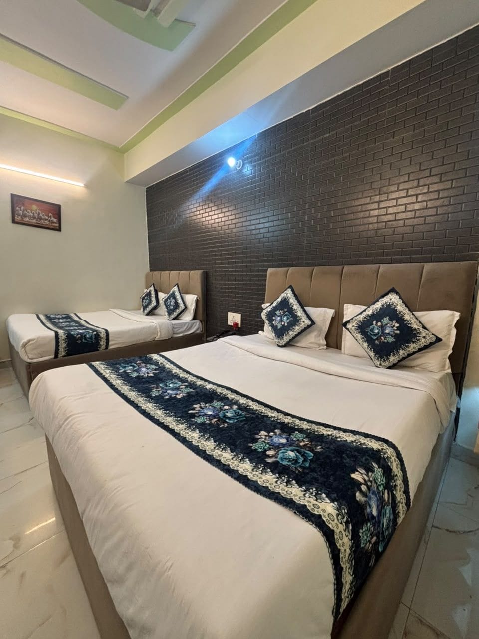 A hotel room with a large bed, a smaller bed, and a brick accent wall.