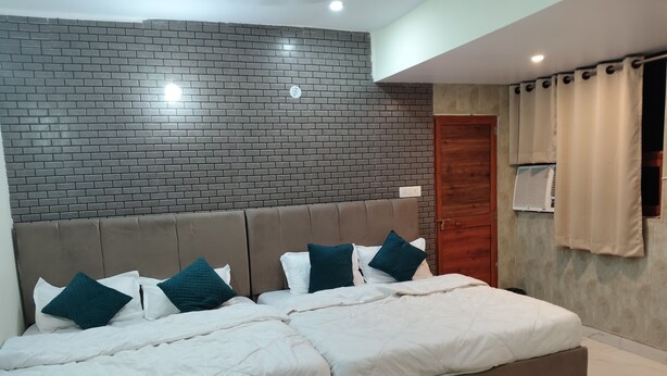 A modern bedroom with a brick-patterned headboard, a large bed with white bedding and teal pillows, and a wooden door. - Hotel AYODHYA HERITAGE (Ayodhya)
