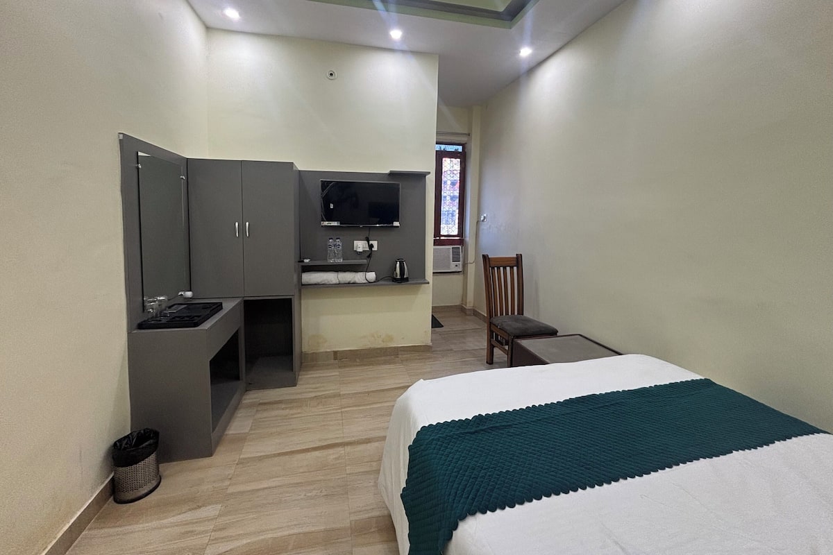 Ein Hotelzimmer mit einem Bett, einem Schreibtisch mit Stuhl, einem Fernseher und einem Fenster mit einem farbigen Glasdekor.