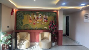 A reception area with a mural, two armchairs, a trash bin, and a potted plant. - Hotel AYODHYA HERITAGE (Ayodhya)