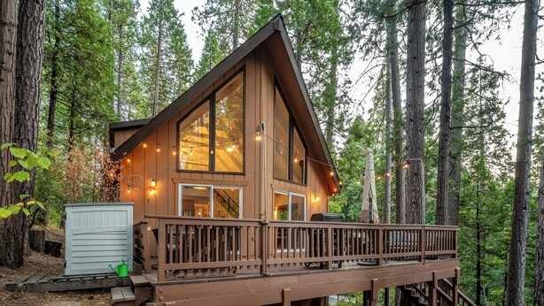 A cabin with a deck, large windows, and a staircase leading to the entrance.