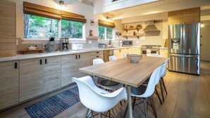 A modern kitchen with a wooden dining table, white chairs, and stainless steel appliances.