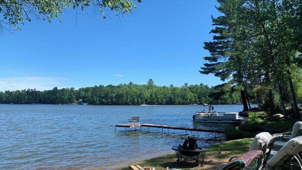 A lakeside setting with a dock, lounge chairs, and a fire pit.