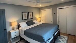 A bedroom with a bed, bedside tables, a ceiling fan, and framed pictures on the wall.