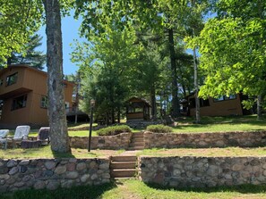 A lodge with stone steps leading to a covered area, surrounded by lush greenery and trees. - Stepaway Vacation Rentals- Circle of Pines Upper Pine Cabin (St.Germain)