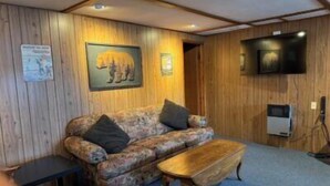 Una habitación con paneles de madera, un sofá estampado con motivos florales, una mesita y un televisor montado.