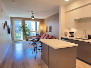A modern kitchen with a central island, a dining area with a table and chairs, and a view of the outside through a large window. - Stylish Apartment Near Disneyland w/ Pool & Gym (Santa Ana)