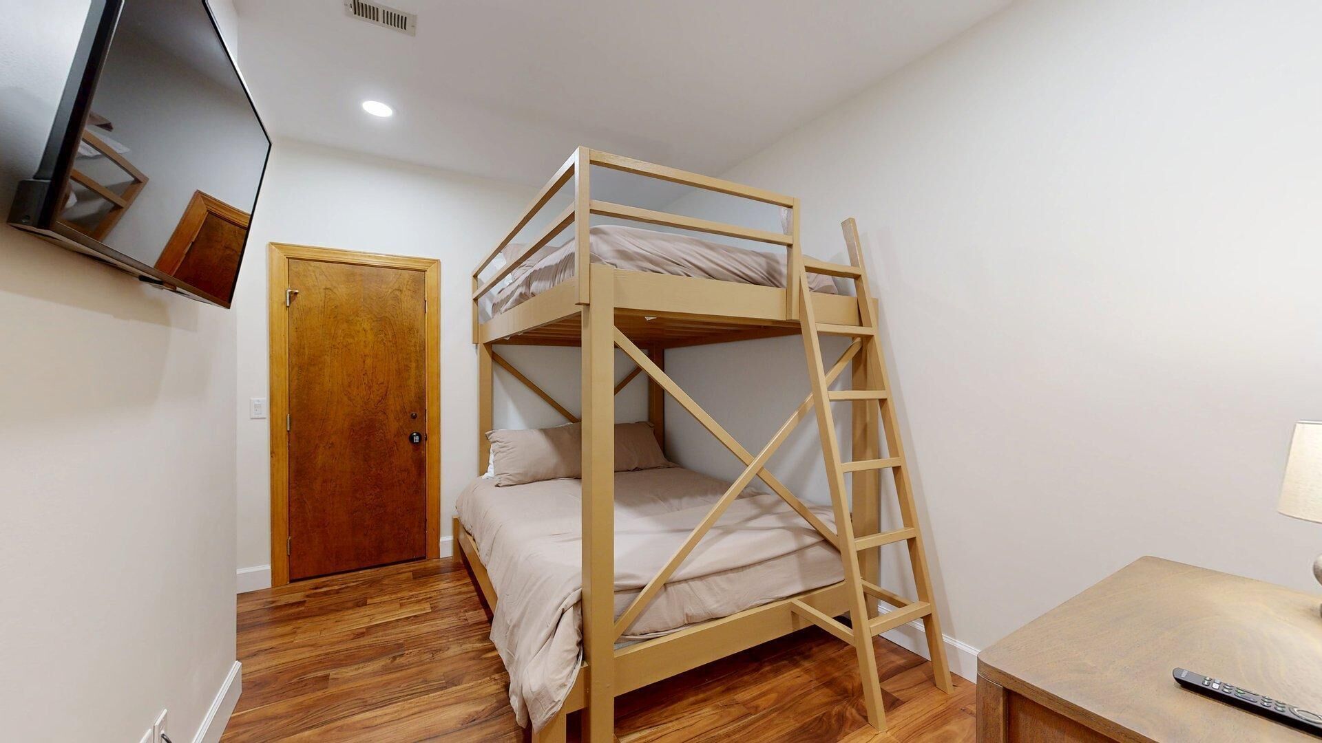 A bunk bed with a ladder, a wooden door, a small table, and a TV mounted on the wall.