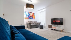 Ein modernes Wohnzimmer mit einem blauen Sofa, einem grauen Sofa, einem Fernseher und einem farbenfrohen abstrakten Gemälde an der Wand.