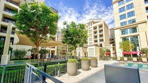 A modern outdoor pool area with a clear sky, surrounded by multi-story buildings with balconies. - WYZ RENT|Earthy Elegant 1BR Surf 2 Creek Beach (Dubai)