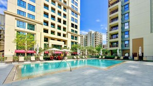A swimming pool surrounded by lounge chairs and umbrellas, with high-rise residential buildings in the background. - WYZ RENT|Earthy Elegant 1BR Surf 2 Creek Beach (Dubai)