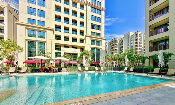 A swimming pool with lounge chairs and umbrellas, surrounded by high-rise buildings. - WYZ RENT|Earthy Elegant 1BR Surf 2 Creek Beach (Dubai)