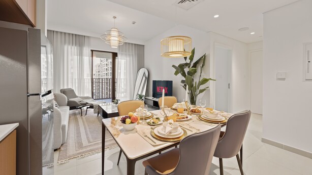 A modern dining area with a table set for four, a sofa, and a large window with curtains. - WYZ RENT|Earthy Elegant 1BR Surf 2 Creek Beach (Dubai)