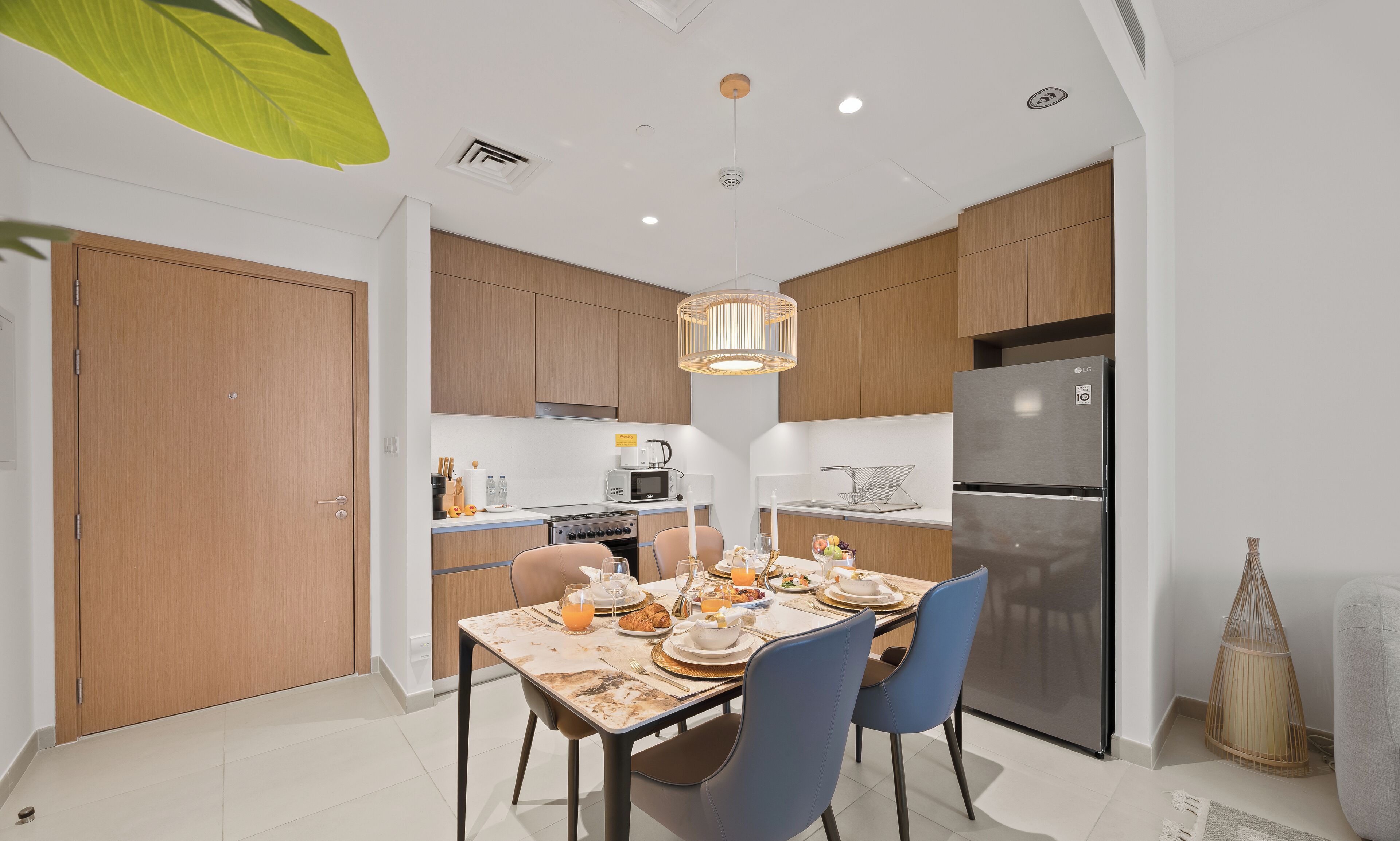 Una cocina moderna con armarios de madera, un refrigerador de acero inoxidable y un comedor con una mesa lista para el desayuno.