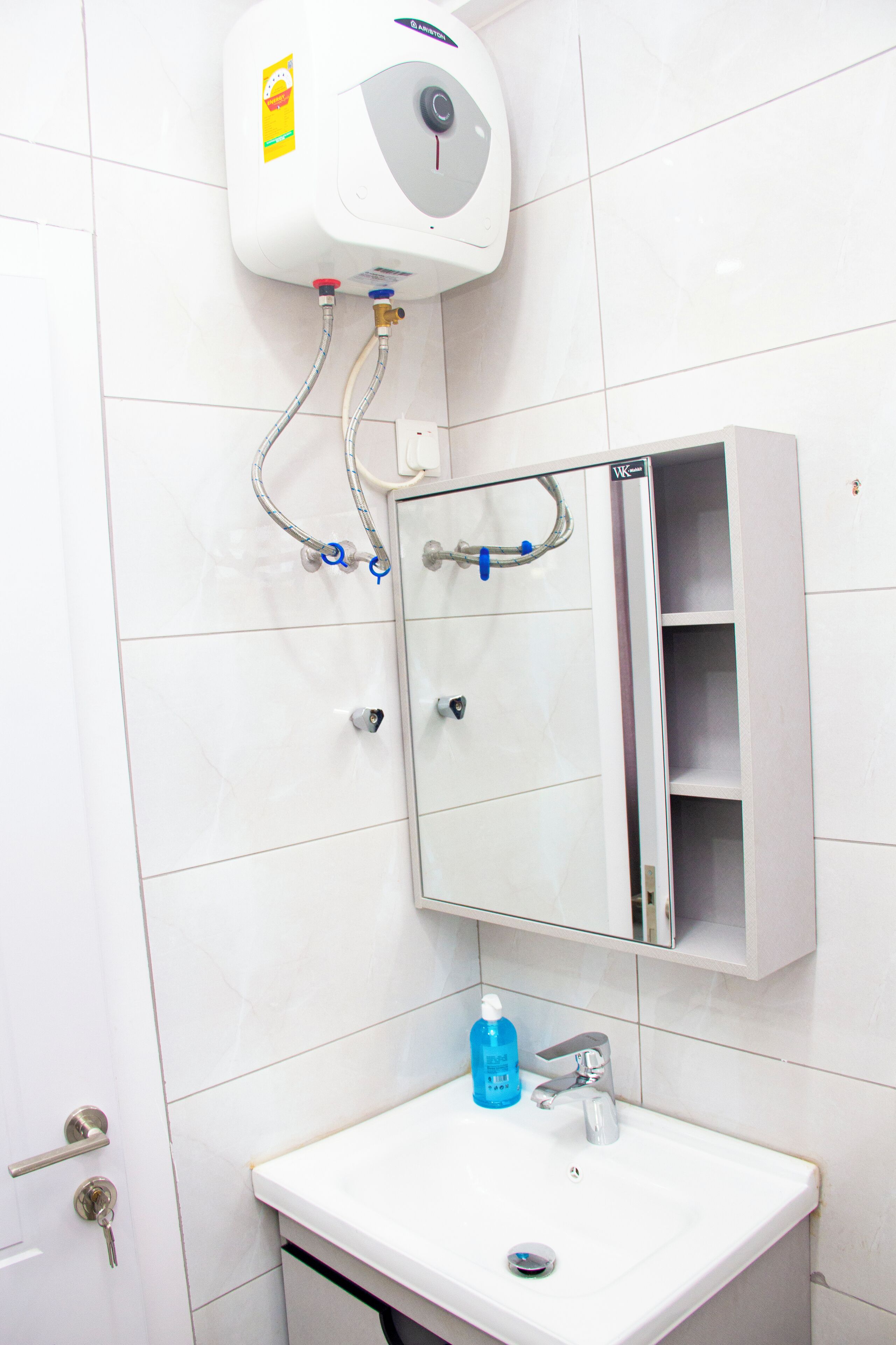 Une salle de bain avec un lavabo blanc, un miroir et un chauffe-eau fixé au mur.