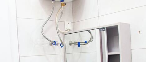 Une salle de bain avec un lavabo blanc, un miroir et un chauffe-eau fixé au mur.