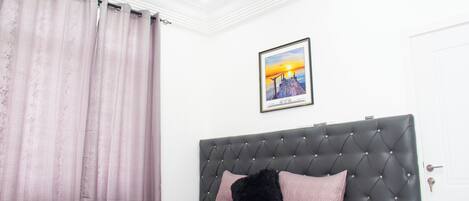A bedroom with a tufted headboard, a bed with patterned bedding, a framed picture on the wall, and a closed door.