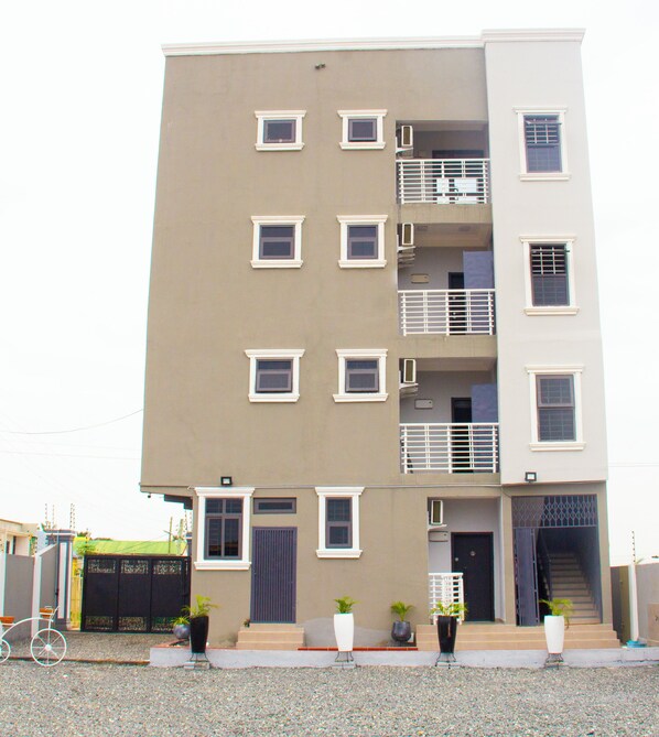 A multi-story building with a flat facade, balconies with railings, and a series of windows.