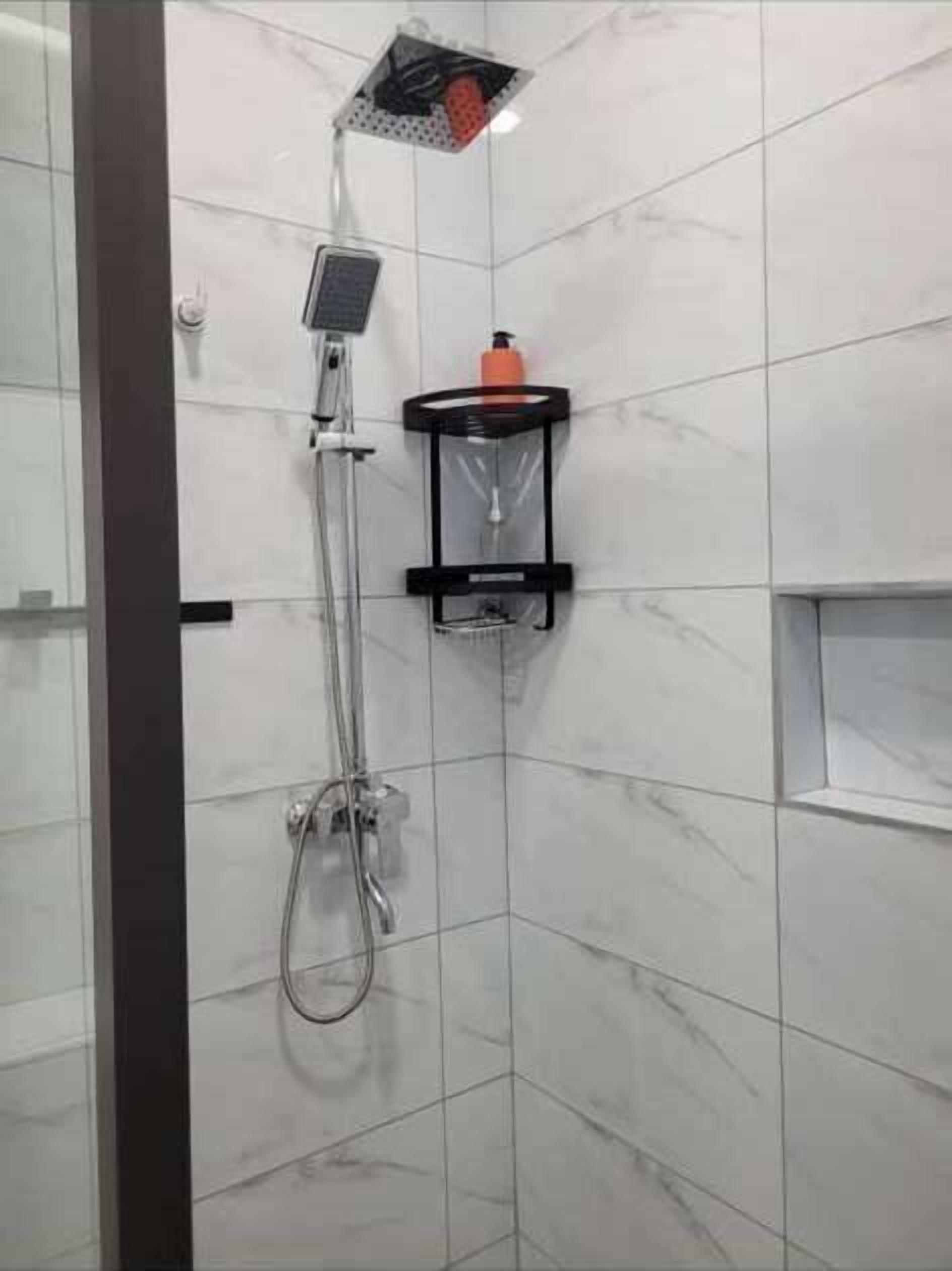 Une douche équipée d’un pommeau de douche à main, d’un distributeur de savon à main et d’un panneau de commande fixé au mur.