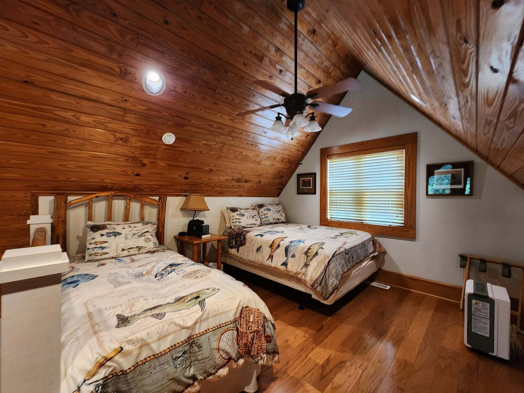 Une chambre avec deux lits, un ventilateur de plafond, une fenêtre avec des stores et un plafond en bois.