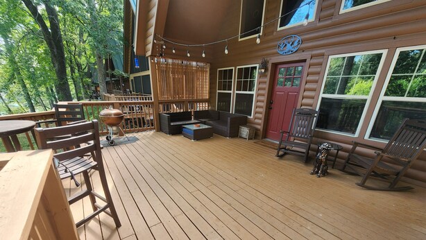 A wooden deck with outdoor furniture, a grill, and a red door.